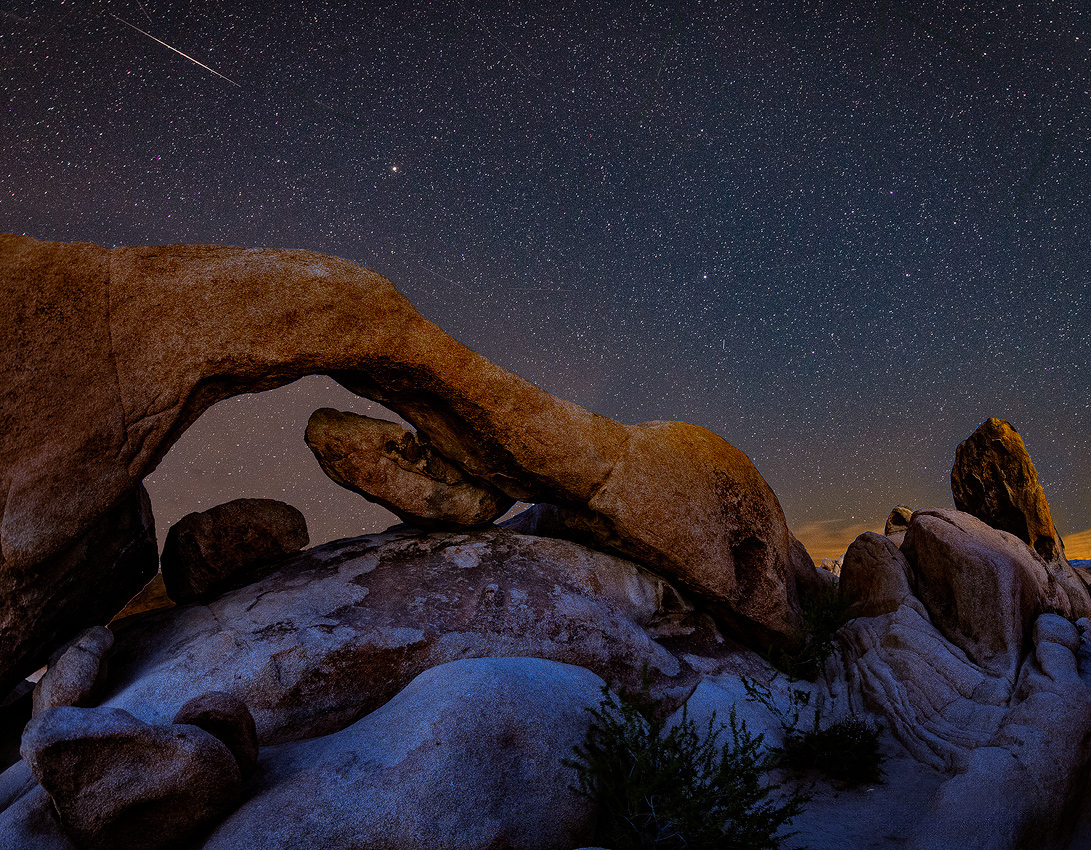 A satellite streaks above Arch Rock in Joshua Tree National Park at night.
